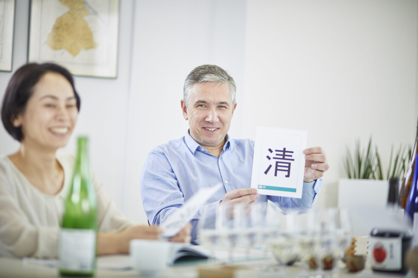 Man and woman in a sake class. The man is holding up a kanji sign.