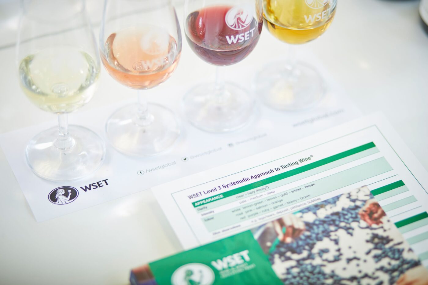Four glasses of various wines with the course material for WSET Level 3 Award in Wines