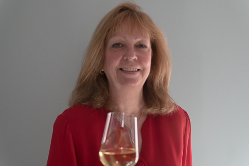 Woman in a red shirt smiling while holding a glass of white wine.