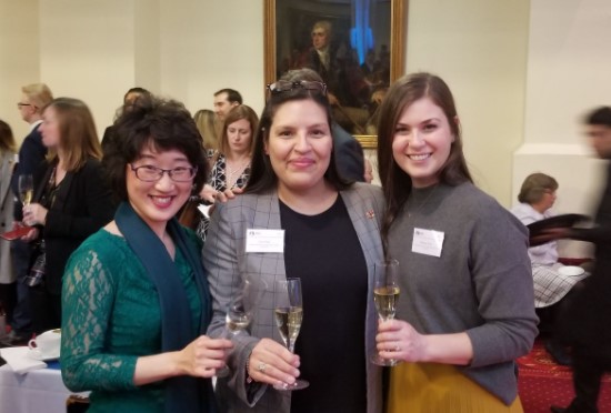 3 women standing together holding glasses of sparkling wine and smiling at the camera