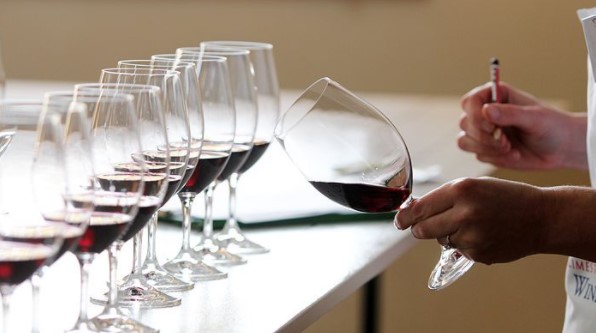 A row of glasses of wine on table with one tilted in a hand for examination