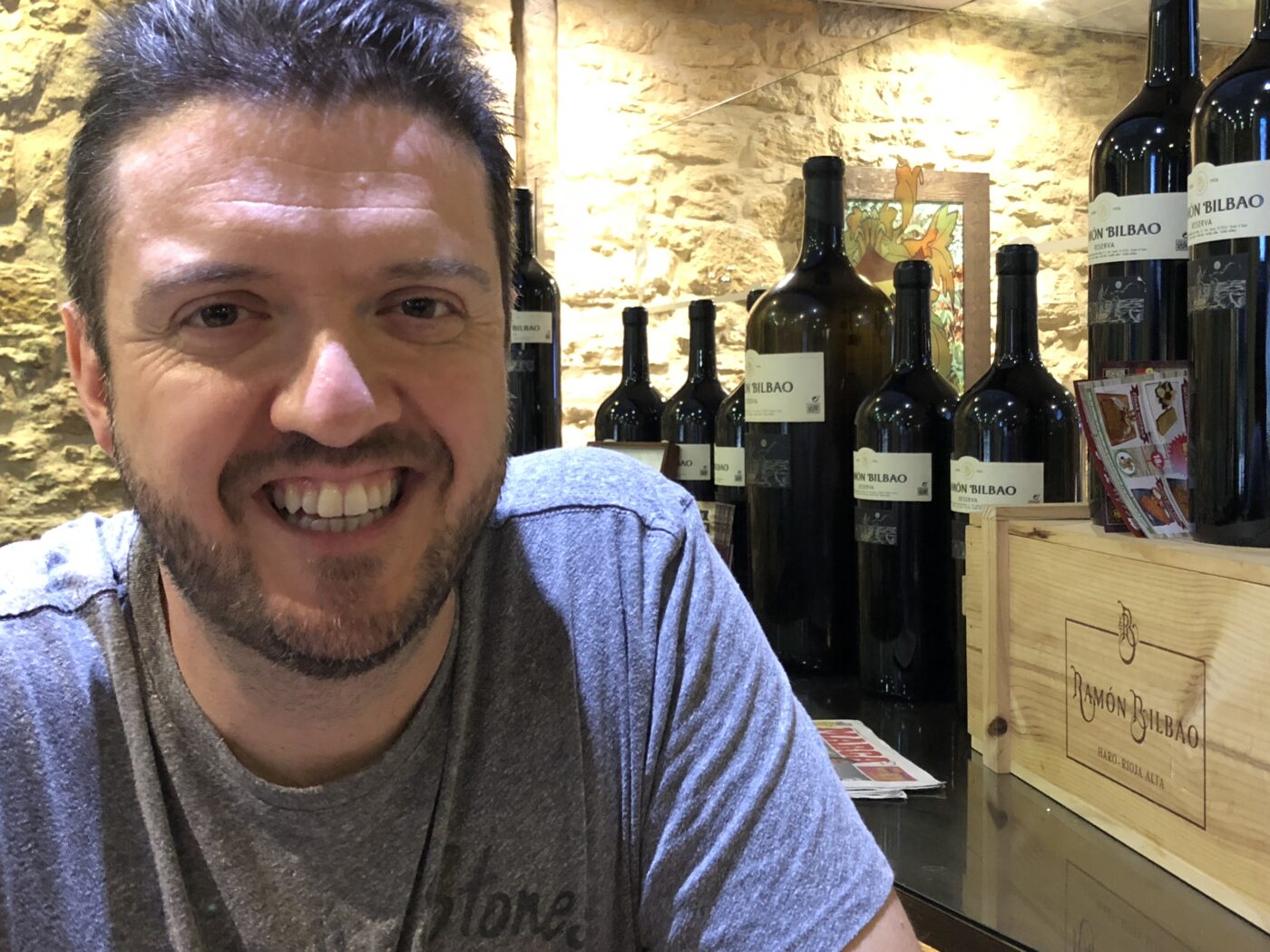 Close up of a man smiling with bottles of wine behind him