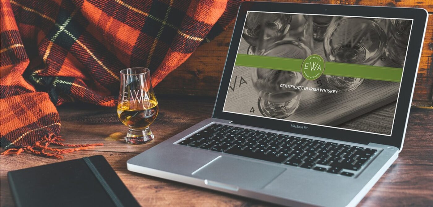 Laptop with black notebook, a glass of whiskey and a green tartan in the background