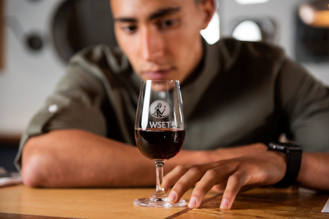 Close up photo of a young man in a great shirt holding and looking at a glass of red wine.