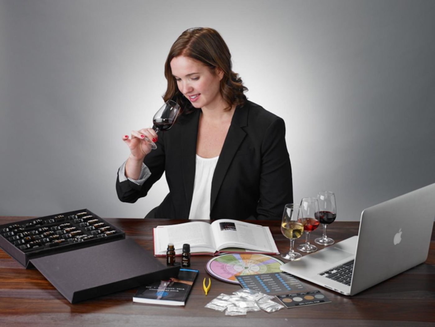 Woman sitting at table smelling a wine with various wine aroma kit tools and scents around her.