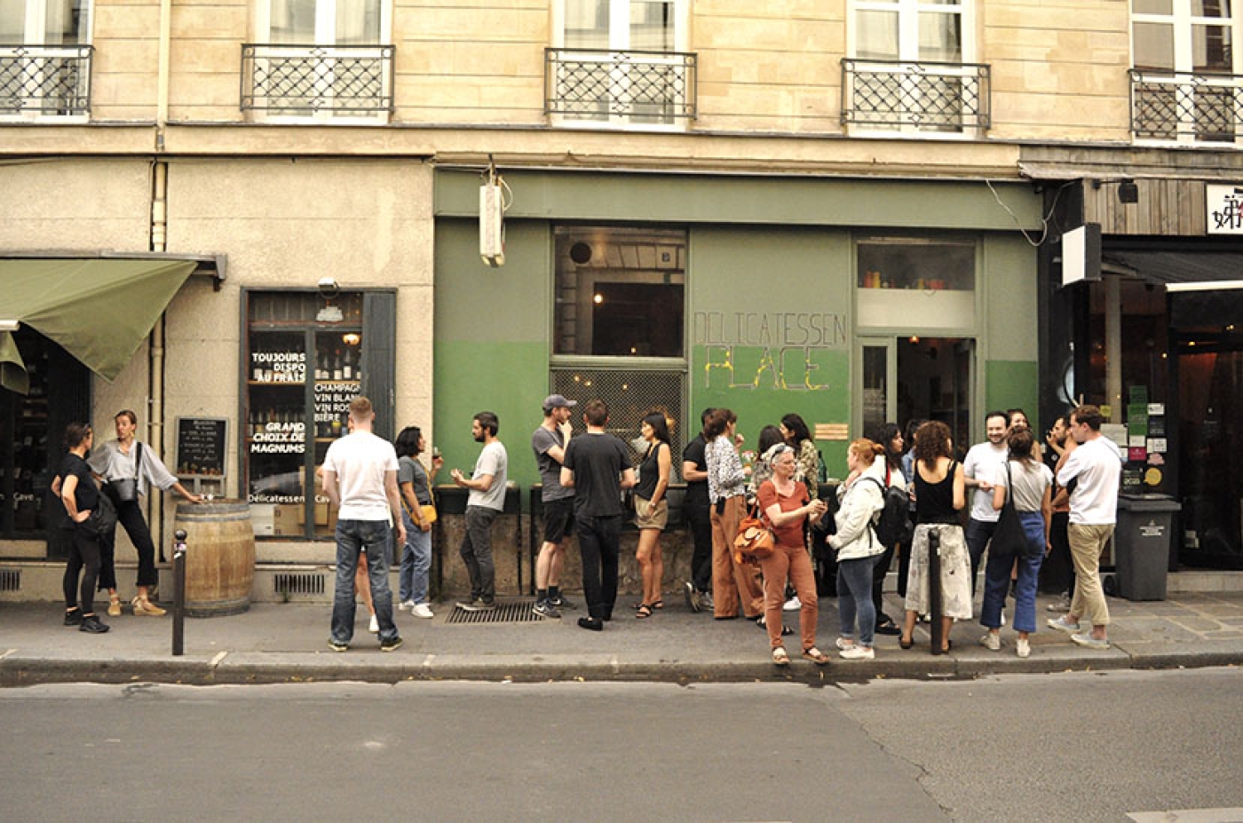 Crowd of people standing and drinking wine outside a wine bar in Paris.