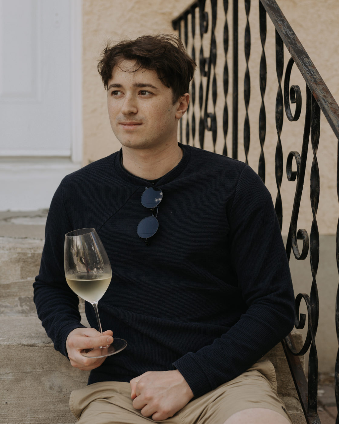 Man sitting on indoor stairs while holding a glass of white wine