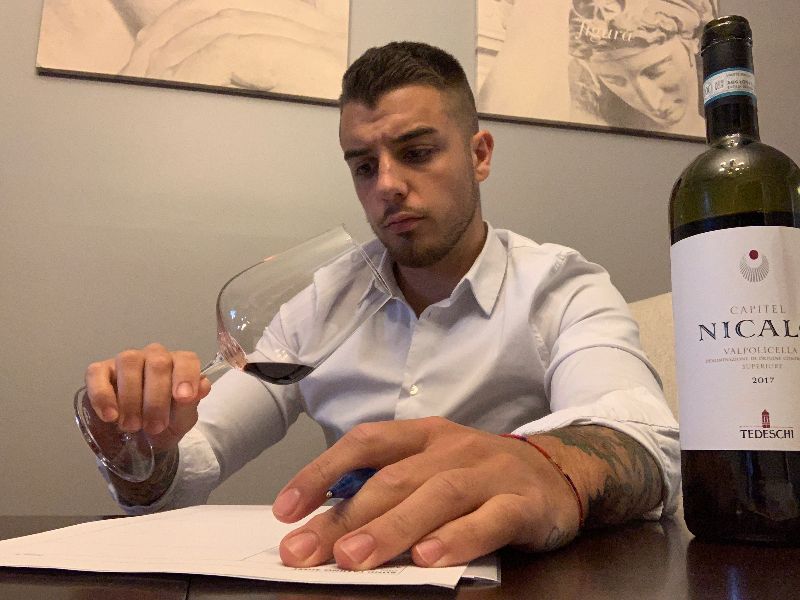Man in a white dress shirt sitting down and looking at a glass of red wine.
