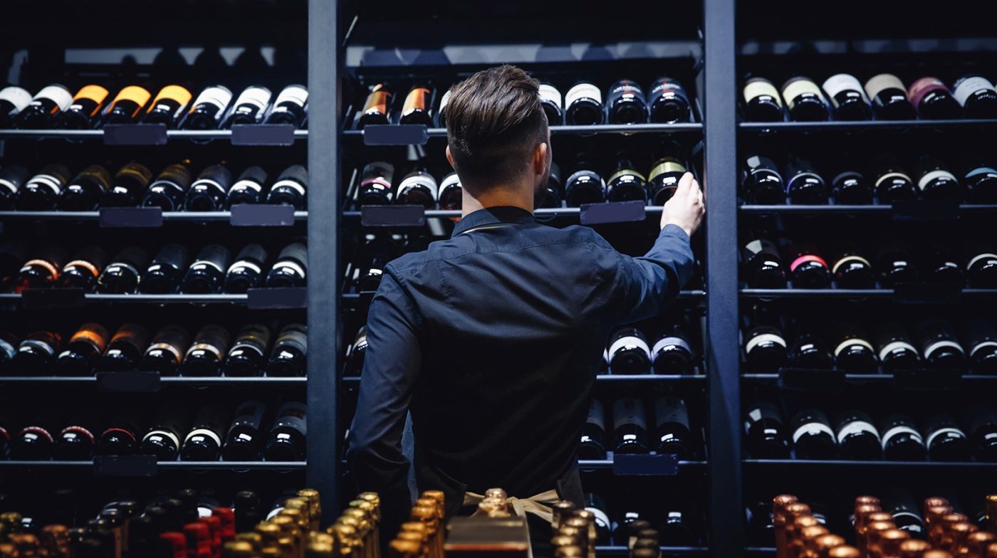 Image of the back of man selecting a bottle of wine off a shelf filled with wine bottles