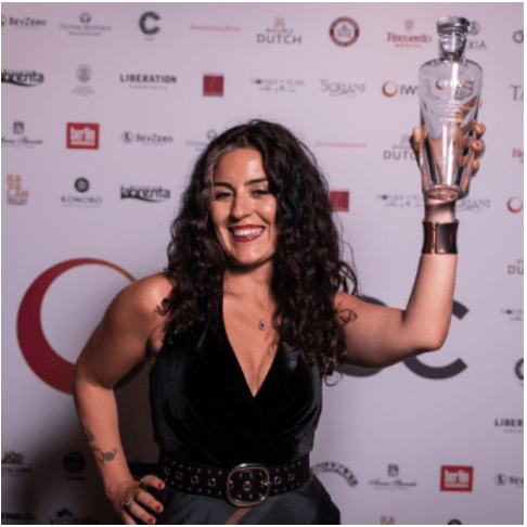 Photo of a woman with long curly hair smiling and holding up a glass trophy.