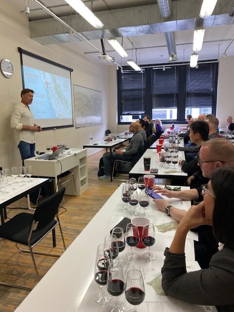 A classroom full of adult students with wines facing a man presenting.