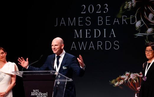 A man in a navy suit with his arms out on a podium on a stage at the 2023 James Beard Book Award ceremony.