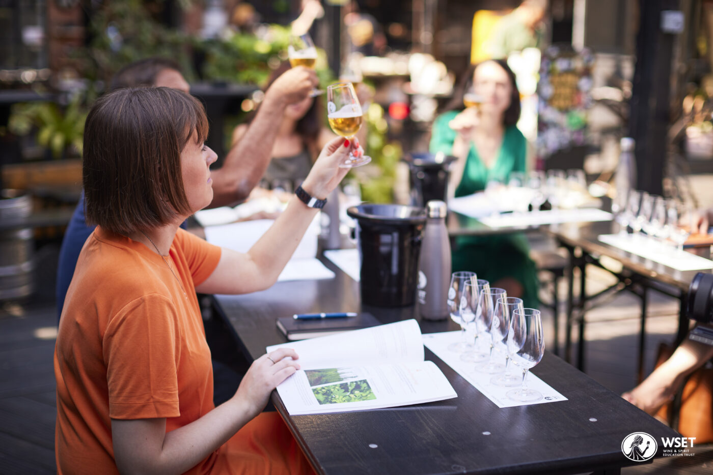 Three people sitting around a table with a flight of beers in different hues. They are each holding up a glass up.