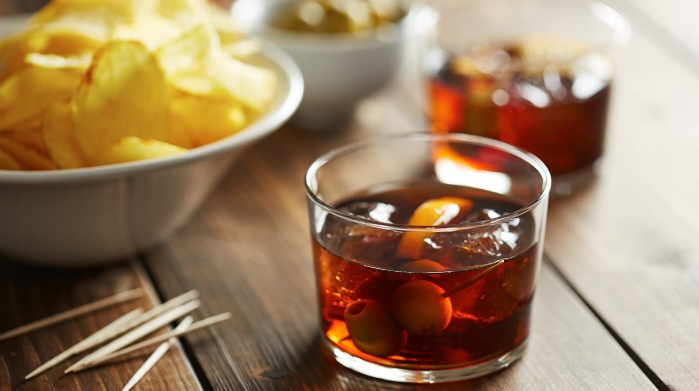 Two glasses of vermouth with appetizers such as olives, potato chips and mussels