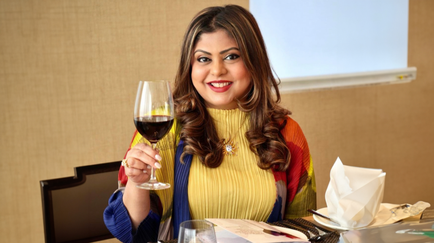 A woman wearing a colourful top smiling while holding up a glass of red wine.